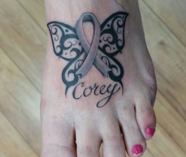 Tatuagem de borboleta tribal com nome e fita no pé 