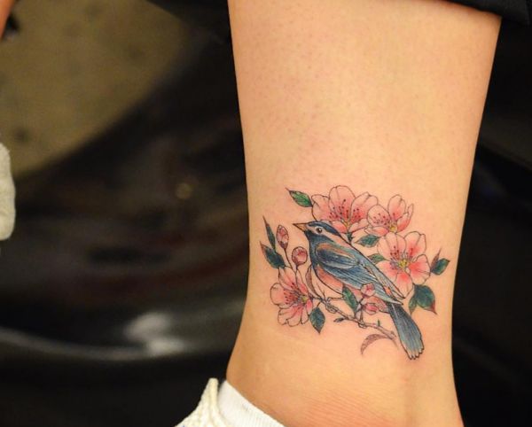 Flores de cerejeira e tatuagem de pássaro no tornozelo 