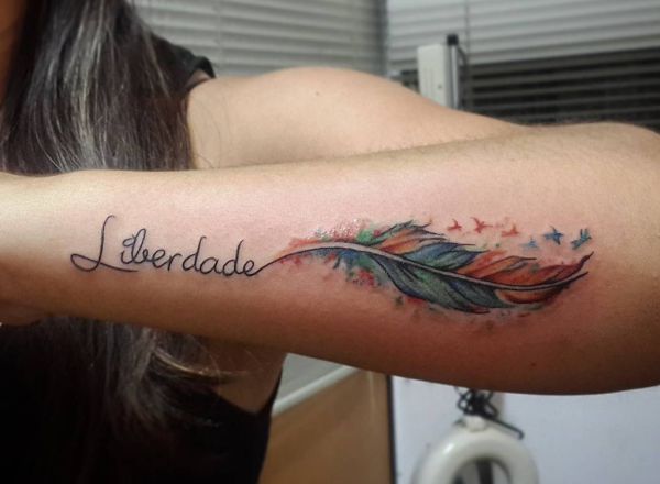 Tatuagem de penas coloridas com provérbios no antebraço 