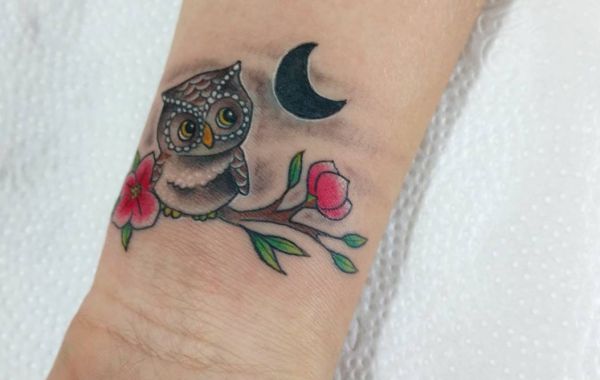 Tatuagem de coruja com lua crescente e flores no pulso 