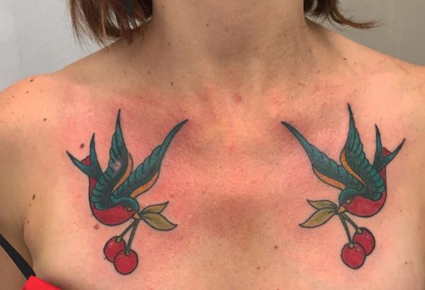 Tatuagem de cereja e desenho de andorinhas no peito de uma mulher 