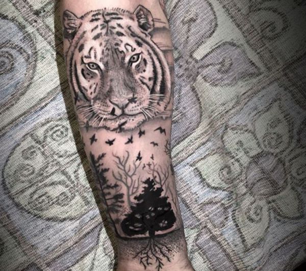 Tigre com tatuagem de pássaro e árvore no antebraço 